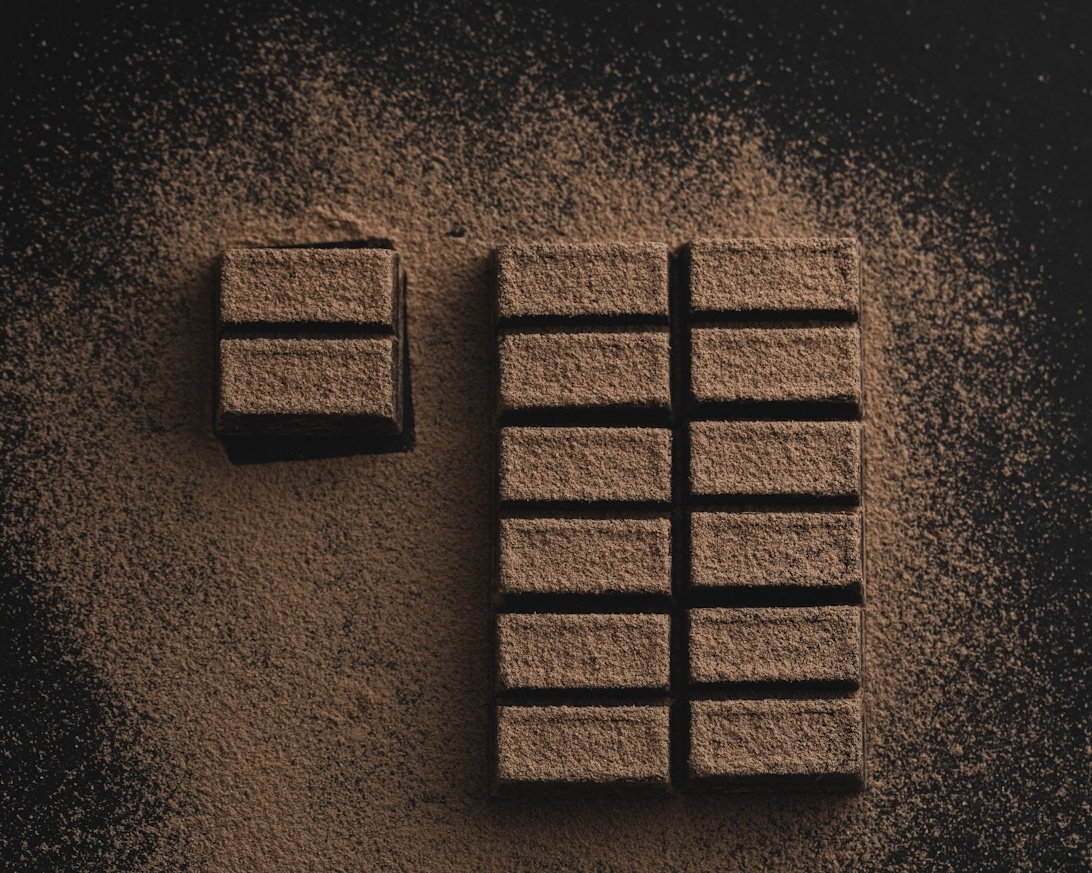 Dark chocolate bars dusted with cocoa powder on a dark surface.