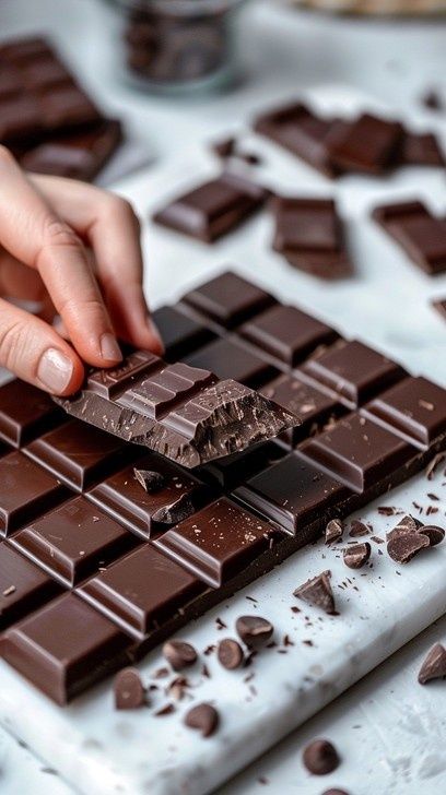 Hand breaking a glossy dark chocolate bar into crisp, layered pieces