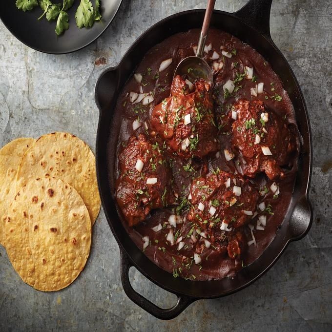 Cast-iron skillet of red mole with onions, herbs, and tortillas